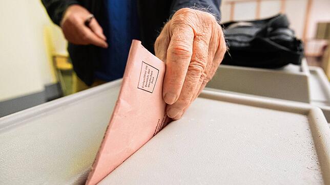 Ein Mann wirft einen Umschlag mit seinen Stimmzetteln in eine Wahlurne (Symbolbild).