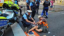 Ein Polizist auf der Charlottenstraße neben einem Demonstranten, der sich mit einer Hand auf der Fahrbahn festgeklebt hat.
