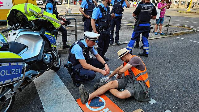 Ein Polizist auf der Charlottenstraße neben einem Demonstranten, der sich mit einer Hand auf der Fahrbahn festgeklebt hat.