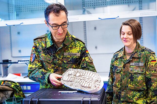 Cem Özdemir begutachtet für eine simulierte Tatort- und Spurensicherung im Rahmen der Wehrübung einen Fußabdruck auf Gips.