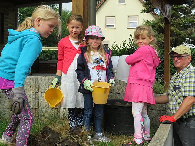 In Teamarbeit sammeln die Kinder die Steine ein und werfen sie in einen Sammelbehälter. Auf dem breiteren Rasenstreifen soll später ein ...