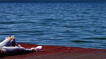 Eine junge Frau &ndash; mit löchriger Hose, versteht sich &ndash; genießt auf einem Steg an einem See den Sonnenschein.
