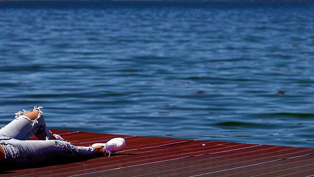 Eine junge Frau &ndash; mit löchriger Hose, versteht sich &ndash; genießt auf einem Steg an einem See den Sonnenschein.