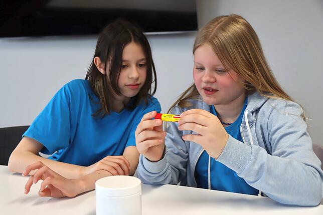 Hanna und Linn (von links) studieren die Aufschrift eines industriell gefertigten Lippenpflegestiftes.