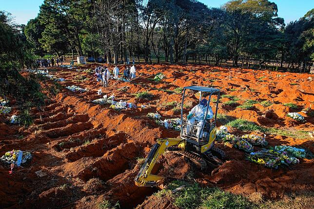 Ein Bagger gräbt in Brasilien während der Corona-Pandemie Gräber auf einem Friedhof.
