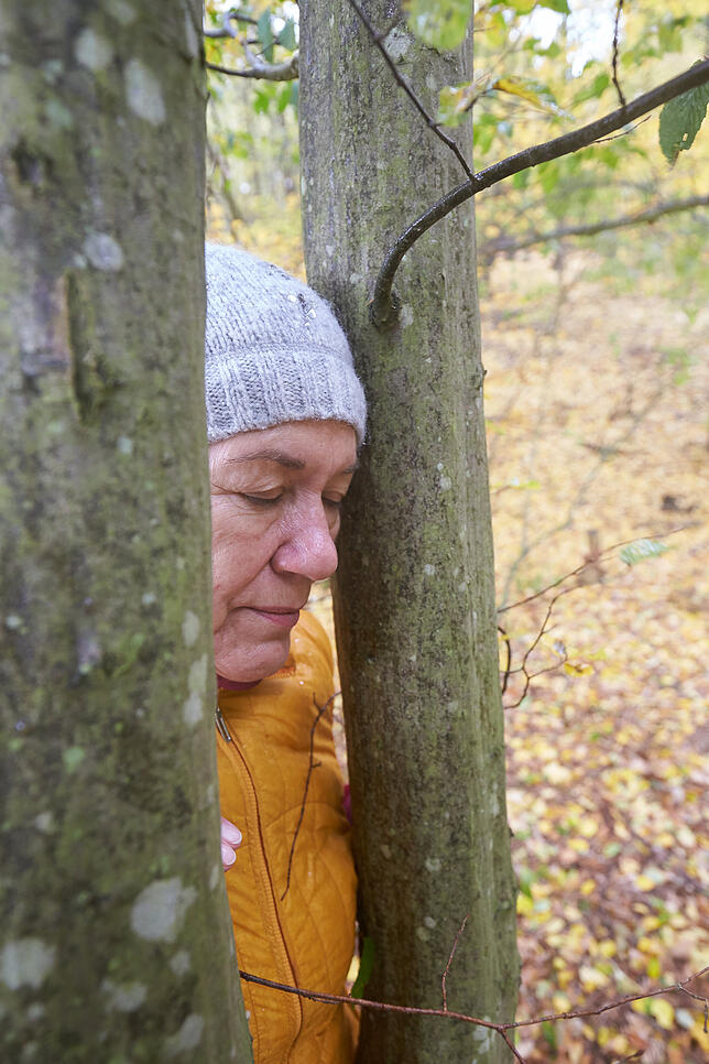 Eine Teilnehmerin eines Kurses im Waldbaden lehnt sich an einen Baum. Die Achtsamkeits-Übungen bilden den Unterschied zum klassischen ...