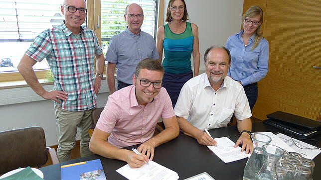 Bürgermeister Fabian Meschenmoser (vorn, links) und Walter Göppel unterzeichnen den Beratungsvertrag. Mit dabei sind (stehend, von ...
