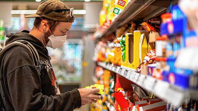 Ein Kunde steht in einem Supermarkt vor einem Regal, und trägt dabei einen Mundschutz. (Symbolbild)