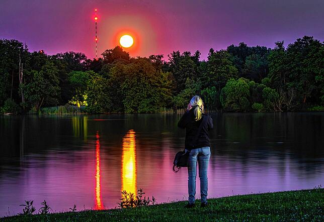 Eine Frau fotografiert den Erdbeermond über dem Schweriner See.