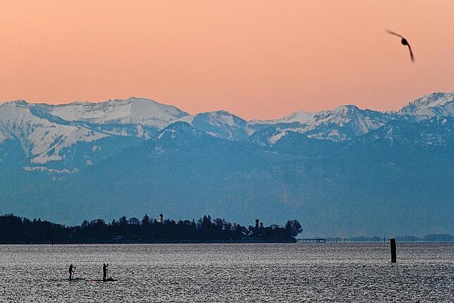 Freizeitaktivitäten gibt es am Bodensee einige: Etwa Stand-Up-Paddeln kurz vor Sonnenaufgang über den Bodensee mit den Alpen im Blick.