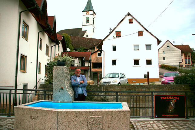 Ortsvorsteher Wolfgang Löhle am Dofbrunen, im Hintergrund steht die Dorfkirche.