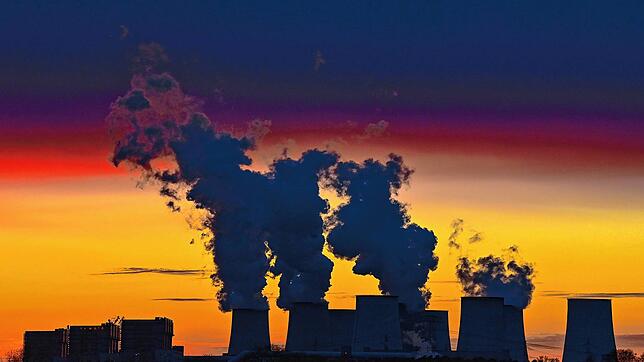Die dampfenden Kühltürme eines Braunkohlekraftwerks in der Lausitz heben sich dunkel vor dem Abendrot ab. Der Klimawandel ist eine ...