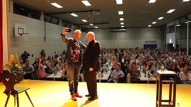 Heinrich del Core und Pfarrer Hans Jürgen Allgaier machen zusammen Selfies auf der Bühne.