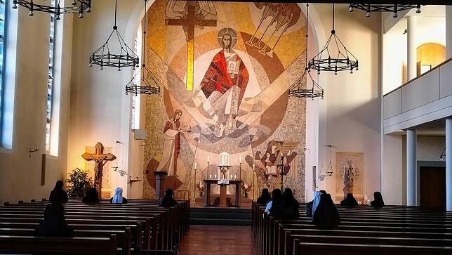 Innenansicht des Anbetungsraums der Klosterkirche Hegne. Der Blick führt auf ein Mosaik des auferstandenen Jesus und vorbei an einigen ...