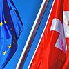 Die Schweizer Flagge hängt neben der EU-Fahne vor blauem Himmel.
