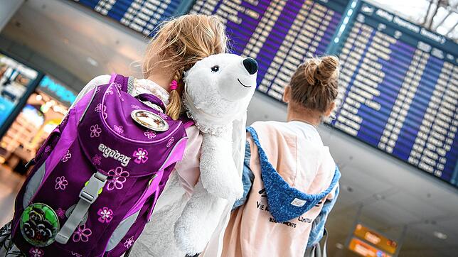 Zwei Mädchen stehen vor dem Abflug in den Urlaub mit ihren Eltern vor einer Abflugtafel am Flughafen in München. Vor Beginn der ...