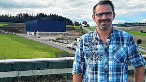 Geschäftsführer Dirk Baumgärtner auf dem Dach des Verwaltungsgebäudes. Im Hintergrund die blaue Halle der Zukunft.