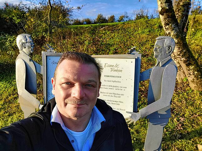 Redakteur Toni Ganter macht ein Selfie vor einer Station des Schwäbisch-Alemannischen Mundartwegs auf dem Höchsten.