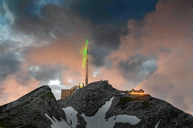 Eine mehrere Kilometer entfernte Kamera hält den grün floureszierenden Laser auf dem Säntis fest, der über der Spitze des Funkturms in ...