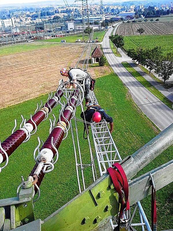 Techniker arbeiten an einer Stromleitung, die zu der im Hintergrund erkennbaren Schaltanlage Laufenburg führt.