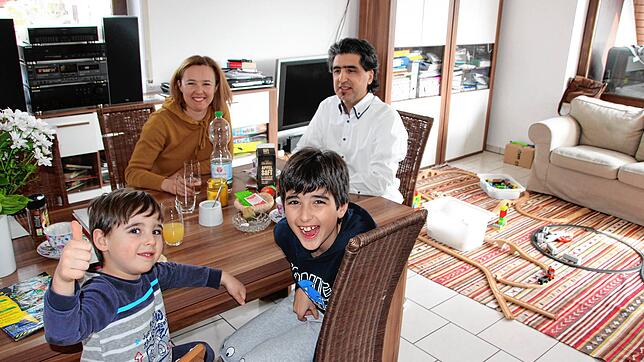 Dilan (vorne links), Kiyan sowie die Eltern Anastasia und Veysel Arslan am Wohnzimmertisch. Rechts die Eisenbahn, mit der die Kinder mit ...