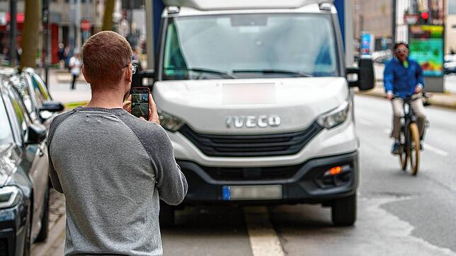 Ein Mann fotografiert ein Lieferservicefahrzeug, das auf dem Radweg parkt. Immer mehr Menschen zeigen Parksünder über Online-Portale an.