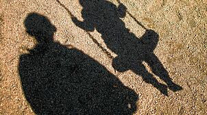 ARCHIV – 27.08.2014, Niedersachsen, Braunschweig: ILLUSTRATION – Der Schatten von einem Mann und einem schaukelnden Kind fallen auf Sand ...