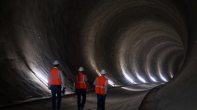 Drei Männer in Warnwesten gehen durch einen Tunnel des Bahnprojektes Stuttgart 21.