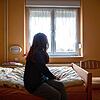 Eine Frau sitzt in einem Frauenhaus auf einem Bett (Symbolbild). Im Kreis Rottweil sind entsprechende Angebote bislang knapp.