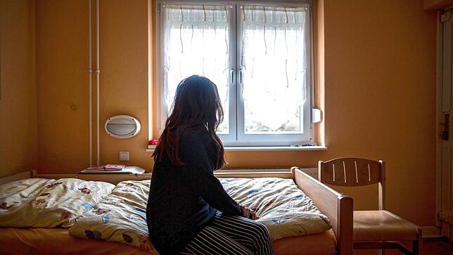 Eine Frau sitzt in einem Frauenhaus auf einem Bett (Symbolbild). Im Kreis Rottweil sind entsprechende Angebote bislang knapp.