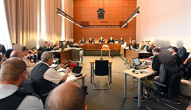 Zu Beginn des Prozesses sitzen elf Angeklagte und Justizbeamte im Landgericht seitlich hinter ihren Anwälten. In der Mitte stehen die ...
