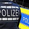 Der Schriftzug Polizei ist auf einem Einsatzfahrzeug und auf der Dienstkleidung eines Polizeibeamten aufgebracht.