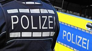 Der Schriftzug Polizei ist auf einem Einsatzfahrzeug und auf der Dienstkleidung eines Polizeibeamten aufgebracht.
