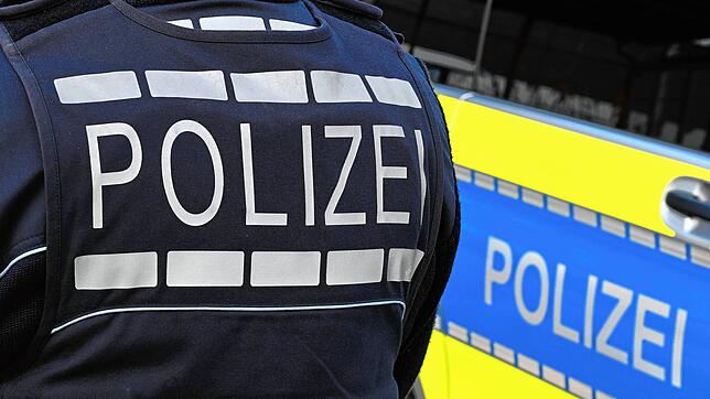 Der Schriftzug Polizei ist auf einem Einsatzfahrzeug und auf der Dienstkleidung eines Polizeibeamten aufgebracht.