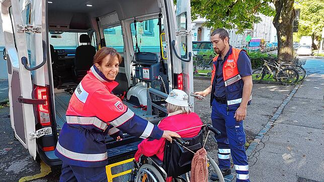 Caroline Pierro und Tobias Hiller schieben Birgit Kirchner in den Malteserwagen und schnallen ihren Rollstuhl an.