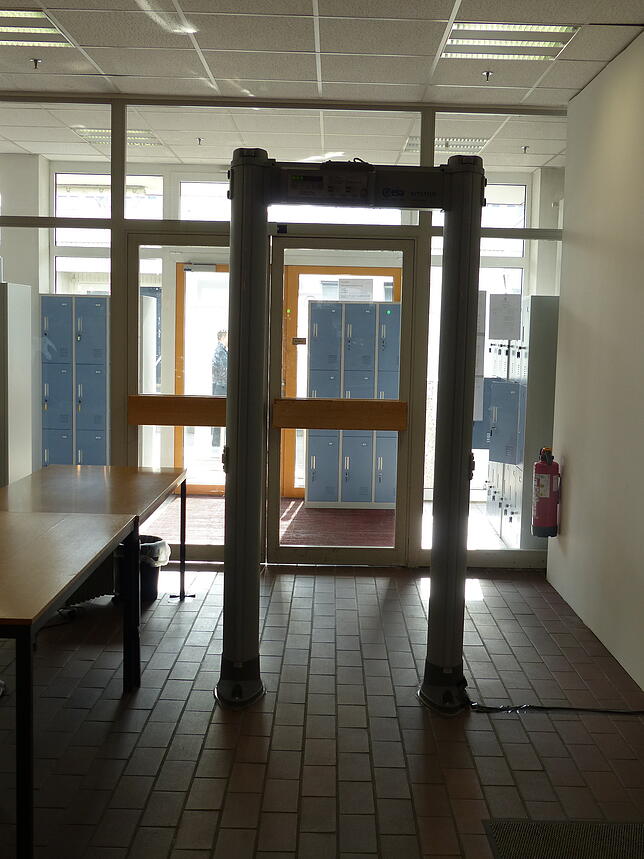 Diese Sicherheitsschranke müssen die Prozessbetiligten passieren. Justizbeamte kontrollieren Taschen und Rucksäcke. Handys, Glasflaschen ...