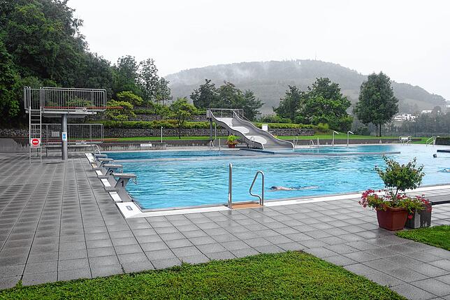 Auch bei weniger gutem Wetter ziehen Schwimmer im 25-Meter-Bescken ihre Bahnen. Im Hintergrund erhebt sich der bereits in der Schweiz ...