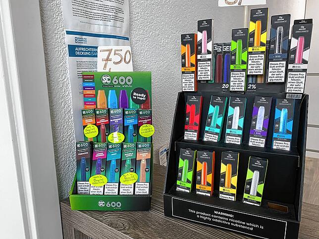 Klein, handlich, bunt, beliebt. Vapes stehen in einem Laden im Ständer. Bei den E-Zigaretten scheiden sich die Geister.
