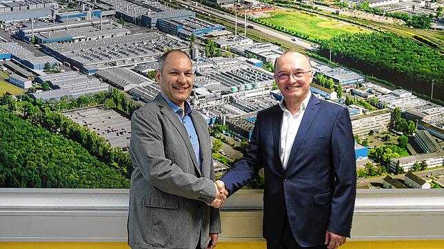 Bernd Honsel (links) übernimmt die Leitung des Singener Walzwerks von Constellium von Robert Gabor. Im Hintergrund ein Luftbild des ...
