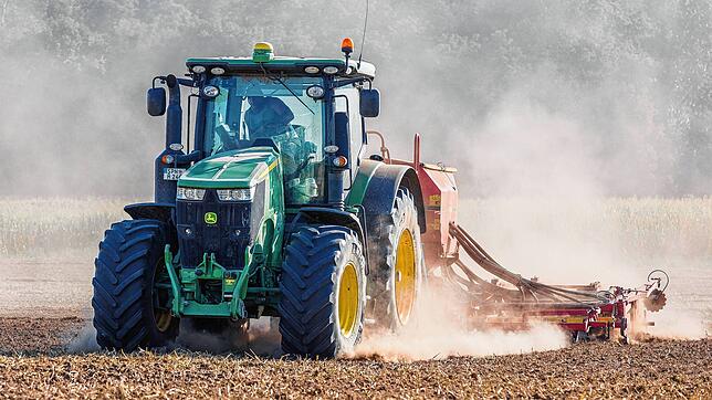 Ein Bauer sät mit seinem Traktor Winterraps auf einem trockenen Feld aus.
