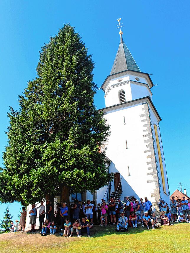 Wegen der Hitze suchen sich einige Gäste ein schattiges Plätzchen an der Kirche.