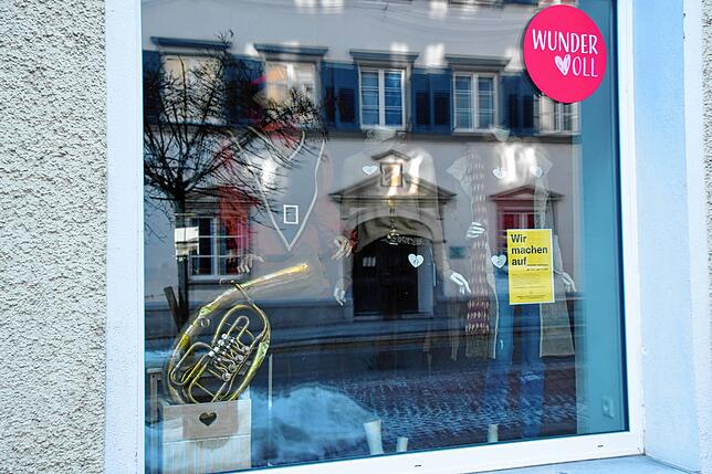 Hinter Schaufenster-Spiegelung bei Wundervoll steht ein Puppe mit dem Häs der Hans Kuony Kapelle und einem Instrument.