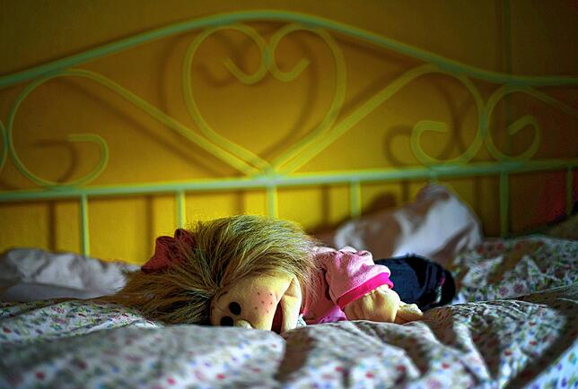 Eine Puppe liegt in einem Kinderzimmer auf dem Bett.