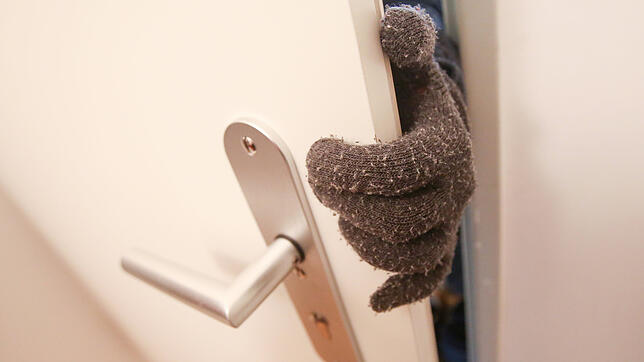 Eine Person, die Stoffhandschuhe trägt, betritt eine fremde Wohnung (gestelltes Foto).