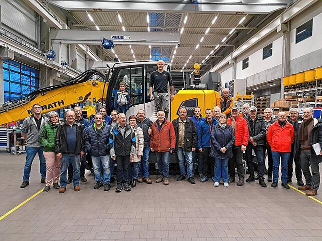 Die Besuchergruppe vor einem von Morath hergestellten Bohrbagger. Oben steht Produktionsleiter Christoph Behringer, links ...