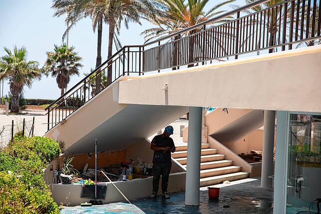 Spanien, Palma: Ein Bauarbeiter steht während der Mittagshitze an einem Lokal am Strand von Arenal im Schatten.
