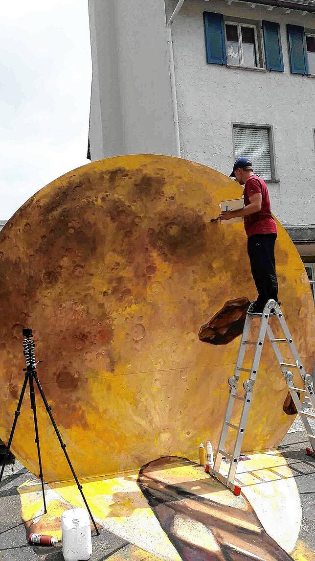 Auf der Leiter malt Nikolaj Arndt an der Sonne für sein großes 3D-Bild auf dem Blumberger Marktplatz.