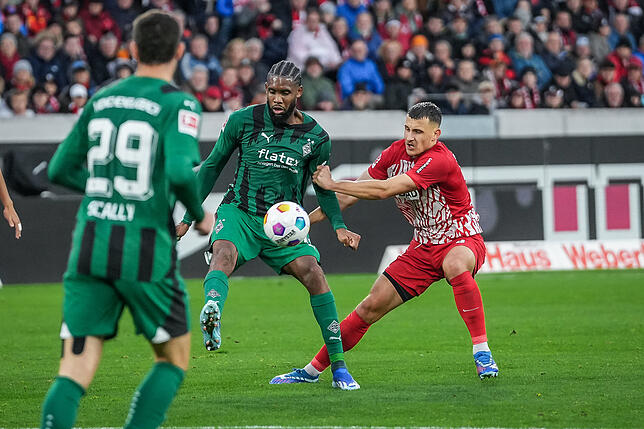 Gladbachs Jordan Siebatcheu (M) wird festgehalten von Freiburgs Maximilian Eggestein (r).