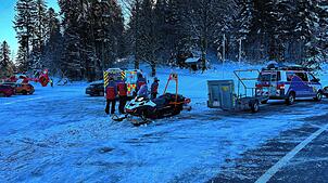 Helfer der Bergwacht kümmern sich um den verunglückten Langläufer. Im Hintergrund links ist ein Schweizer Rettungshubschrauber zu sehen.