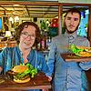 Mia Wagner und Parsival Bauer auf dem Weg, Gästen einen vegangen Burger und ein Schnitzelbrot zu servieren.